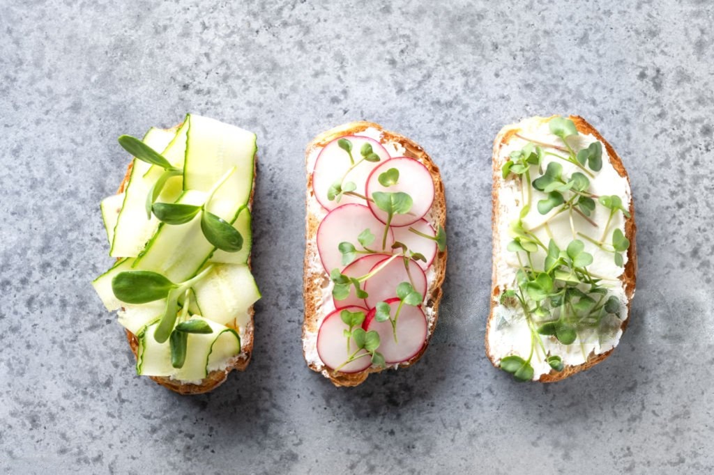Tres tostadas con verduras y microgreens sobre piedra